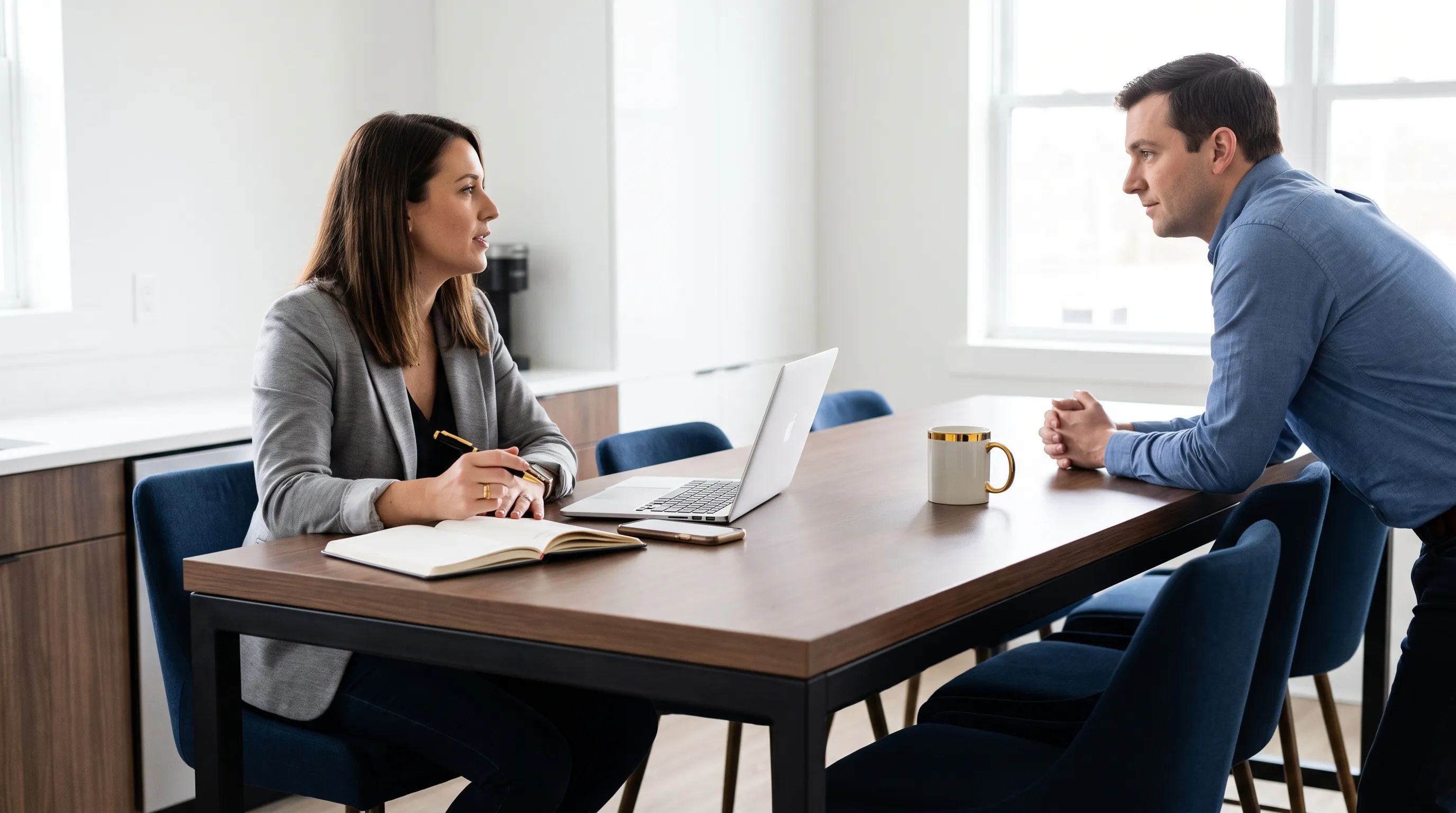 A founder checks an automation proposal at a kitchen table in a real office break area while a colleague waits nearby.
