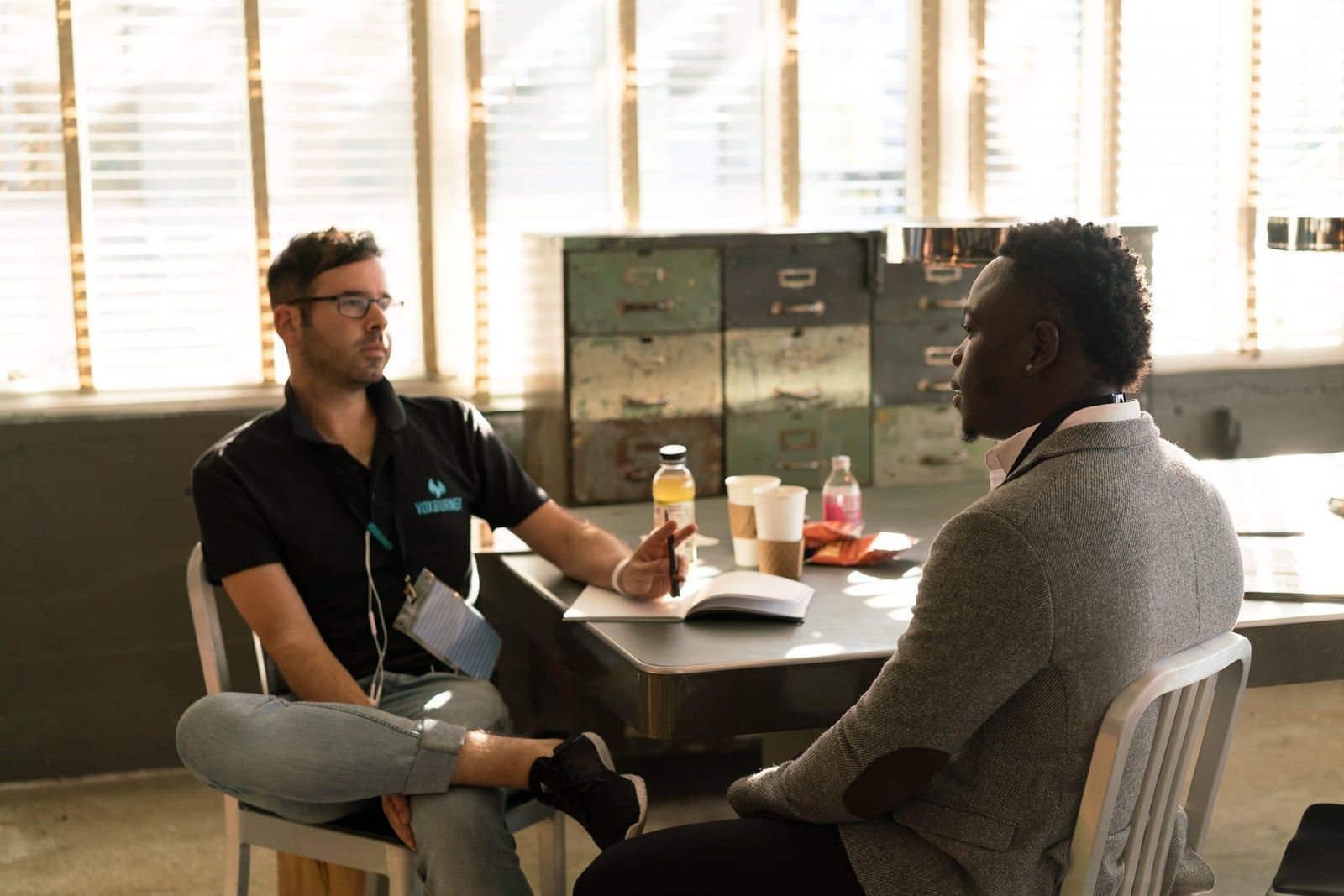 Two colleagues talking across a table, one asking how the other did it
